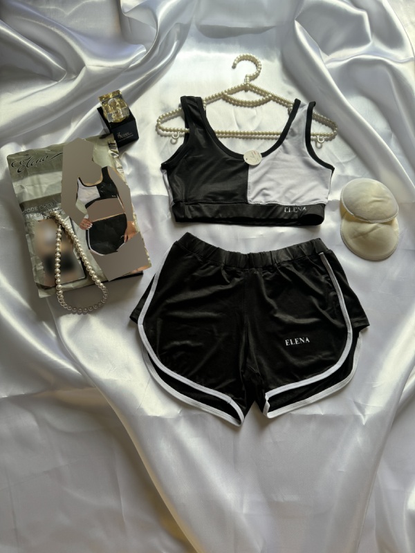 ست ورزشی زنانه شامل نیم‌تنه و شورتک مشکی سفید همراه با بسته‌بندی عکس‌دار، پد اضافی، چوب‌لباسی مرواریدی و عطر بر زمینه ساتن براق