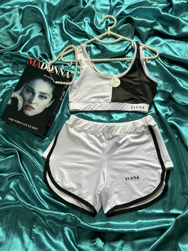 نمای ست ورزشی زنانه شامل نیم‌تنه و شورتک سفید مشکی با طرح اسپرت برند ELENA روی زمینه ساتن سبز