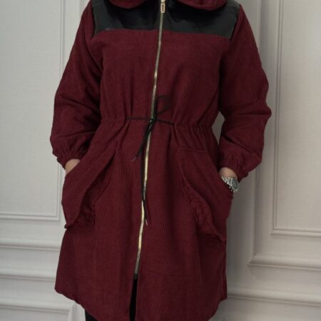 مانتو زنانه مخمل کبریتی ریزباف رنگ زرشکی با نمای روبه‌رو، دارای کلاه، زیپ فلزی و سرشانه چرم مشکی، مدل کمر گت‌دار و مچ کش‌دار، مناسب استایل دانشجویی و روزمره